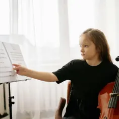 Dziewczynka z wiolonczelą, pięknym instrumentem, wskazuje palcem na nuty.