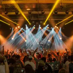Koncert z tłumem podnoszącym ręce. Na scenie artysta, którego pseudonim jest nieznany, w otoczeniu świateł.