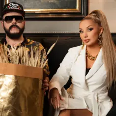 Donatan i Cleo, artystyczny duet, prezentuje złote kłosy. On w czapce i okularach, ona w białej marynarce i z bogatą biżuterią.