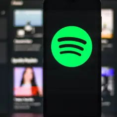Telefon z logo Spotify na ekranie, w tle widoczne inne playlisty.
