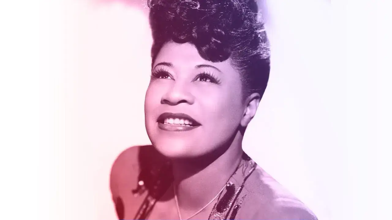 Ella Fitzgerald, wokalistka jazzowa, z uśmiechem patrzy w górę, jej charakterystyczna fryzura i makijaż podkreślają jej piękno.