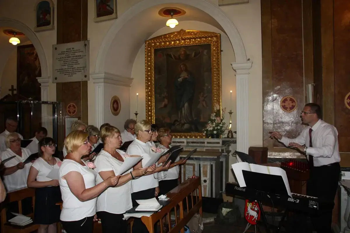 Chór śpiewa pieśń gloria w kościele, dyrygent wskazuje rytm.
