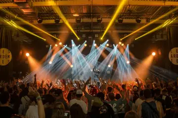 Koncert z tłumem podnoszącym ręce. Na scenie artysta, którego pseudonim jest nieznany, w otoczeniu świateł.
