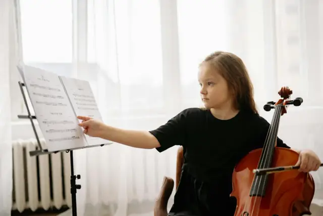 Dziewczynka z wiolonczelą, pięknym instrumentem, wskazuje palcem na nuty.
